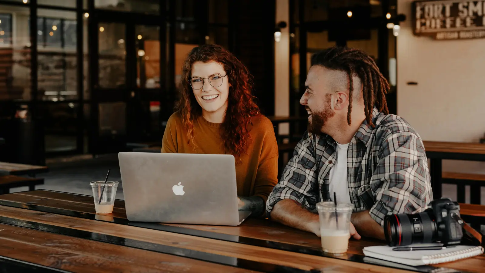 Dwoje młodych ludzi pracuje przy laptopie w kawiarni, omawiając kreację email marketingową i przygotowując skuteczną kampanię.